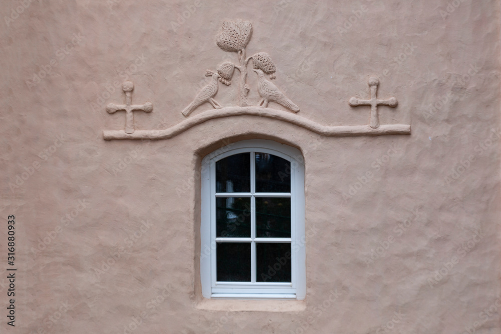 Fragment of the wall of an old church with a window decorated with a bas-relief in the form of two birds
