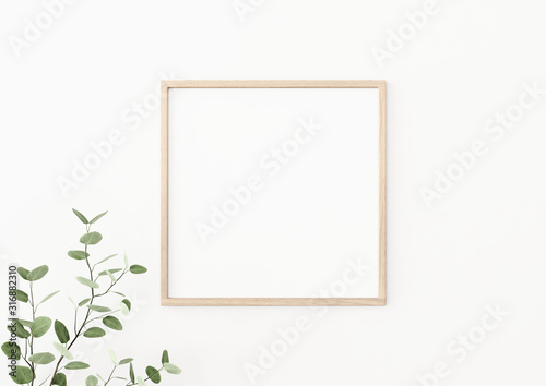 Interior poster mockup with square wooden frame on empty white wall decorated with plant branch with green leaves. 3D rendering, illustration.