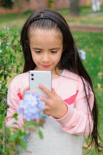 beautiful Latin American Colombian girl takes a picture of the flowers in her home garden with her cell phone