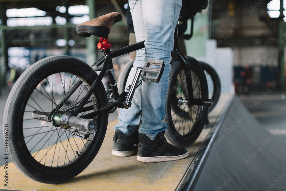 Young male staying with his bike on the ramp. Unrecognizable BMX riders is performing tricks in indoor skatepark. BMX freestyle. Extreme sport.