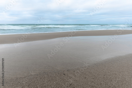 landscape of wide sandy beach by the cold Baltic sea in cloudy weather at long exposure