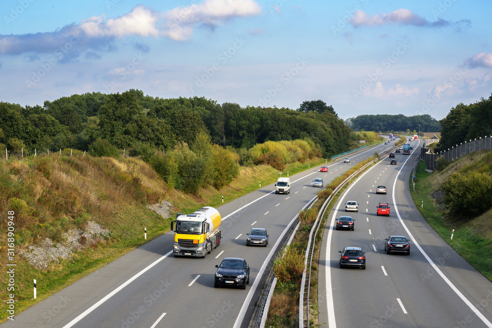 Cars and trucks are driving on the highway through a country landscape, transport and environment concept, blue sky with clouds and copy space