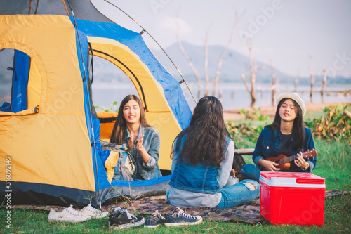 Blurry image of group tourists are enjoying singing in the camping tent amid of warm sunlight by lake in the morning.