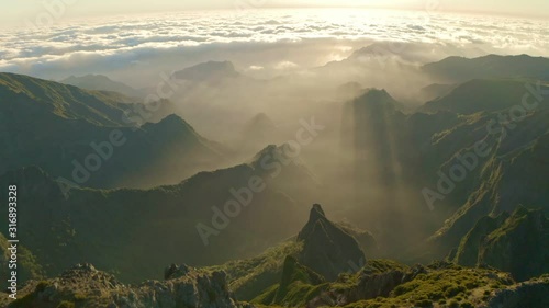 Drone footage of Pico do Arieiro in the island of Madeira, Portugal during a beautiful warm sunset shining over green mountain peaks, valleys, and a cloudy horizon photo