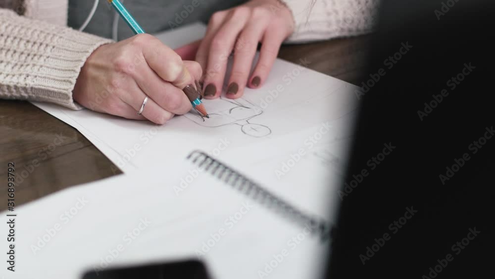 Fashion designer drawing model for clothes sketch. Hand of female tailor drawing pattern at paper in her studio Fashion designer drawing model for clothes sketch. Hand of female tailor drawing pattern at paper in her studio