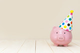 Pink piggy bank with birthday cap on beige background