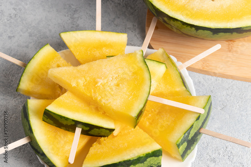 Slices of yellow watermelon on wooden sticks on a dish on the table