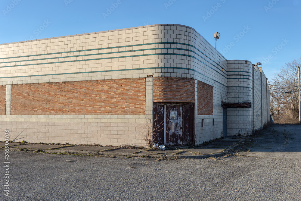 Obraz premium Long abandoned large brick retail building with rounded corners and weed covered sidewalks