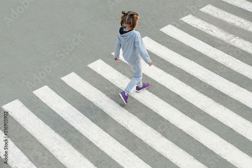 In the summer on the street at the pedestrian crossing kid girl in fashion clothes cross the road. From top view. Shadow at zebra crossing