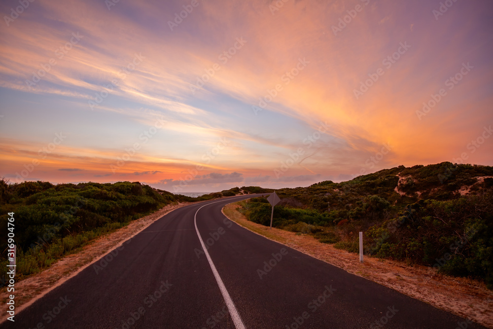 Scenic road winding into the distance near the ocean at beautiful sunset