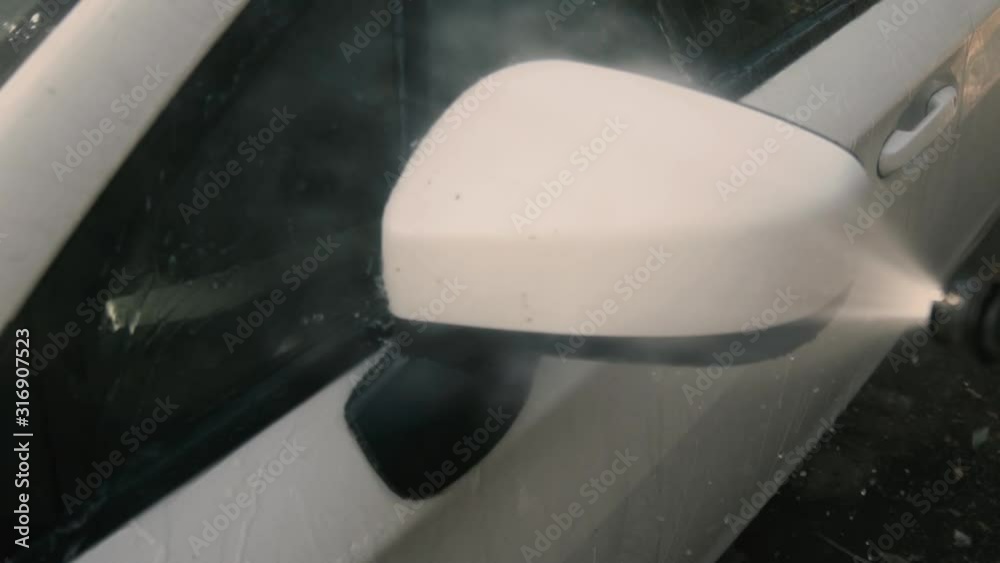 Male cleaning a white car with a pressure washer Male cleaning a white car with a pressure washer