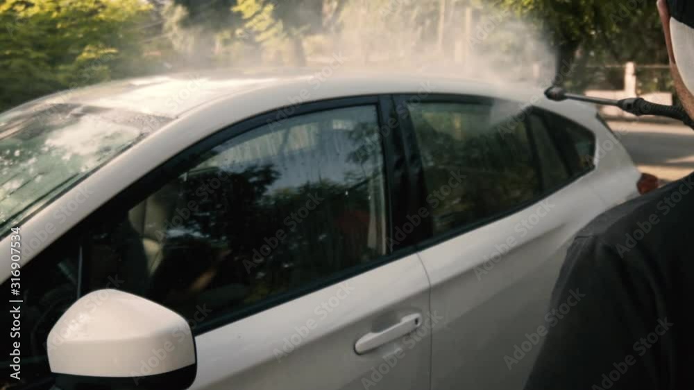 Male cleaning a white car with a pressure washer