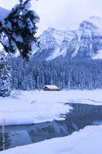 Wooden cabin surrounded by snow covered trees and mountains on shore of Lake Louise near popular Fairmont hotel, Banff National Park, Alberta, Canada 