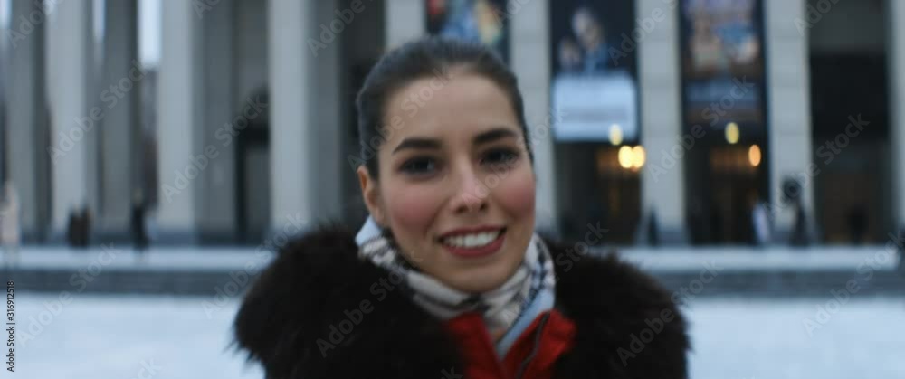 Portrait of a beautiful caucasian girl in red jacket walking in the street or park in winter, turns into camera and smiling. Anamorphic lens, handheld shot Portrait of a beautiful caucasian girl in red jacket walking in the street or park in winter, turns into camera and smiling. Anamorphic lens, handheld shot