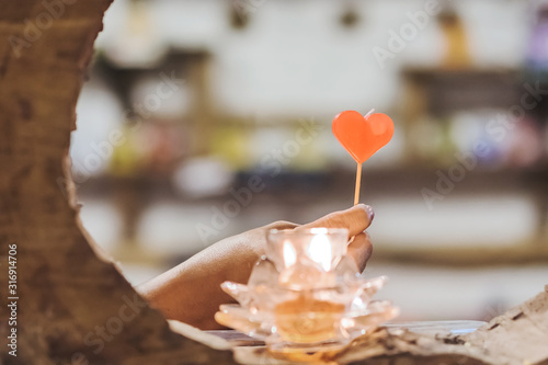 A red heart shaped candle in a woman's hand with candlelight in many small glass cups. A valentine's day background.