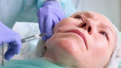 Middle aged woman 50 getting a lifting injection of an injection of hyaluronic acid into the face by a doctor cosmetologist. Cosmetic procedure. close-up photo