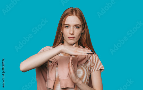 Time out ! Beautiful young red haired woman with freckles showing time out with hand looking at camera seriously against blue background. photo