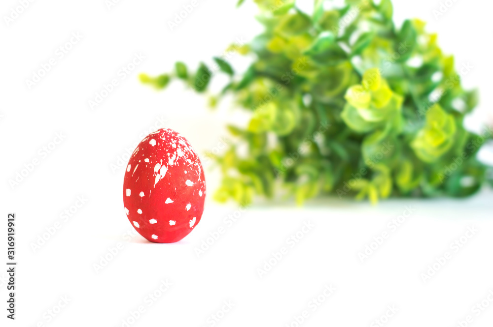 A red Easter egg on a white background and a branch of green in the background. A red Easter egg on a white background and a branch of green in the background.