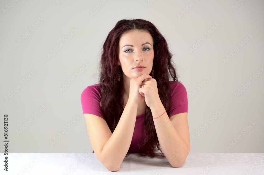 The model smiles and makes a financial report. Portrait of a pretty slender brunette woman in a pink dress and with brown hair sitting at a table on a white background in the studio. The model smiles and makes a financial report. Portrait of a pretty slender brunette woman in a pink dress and with brown hair sitting at a table on a white background in the studio.