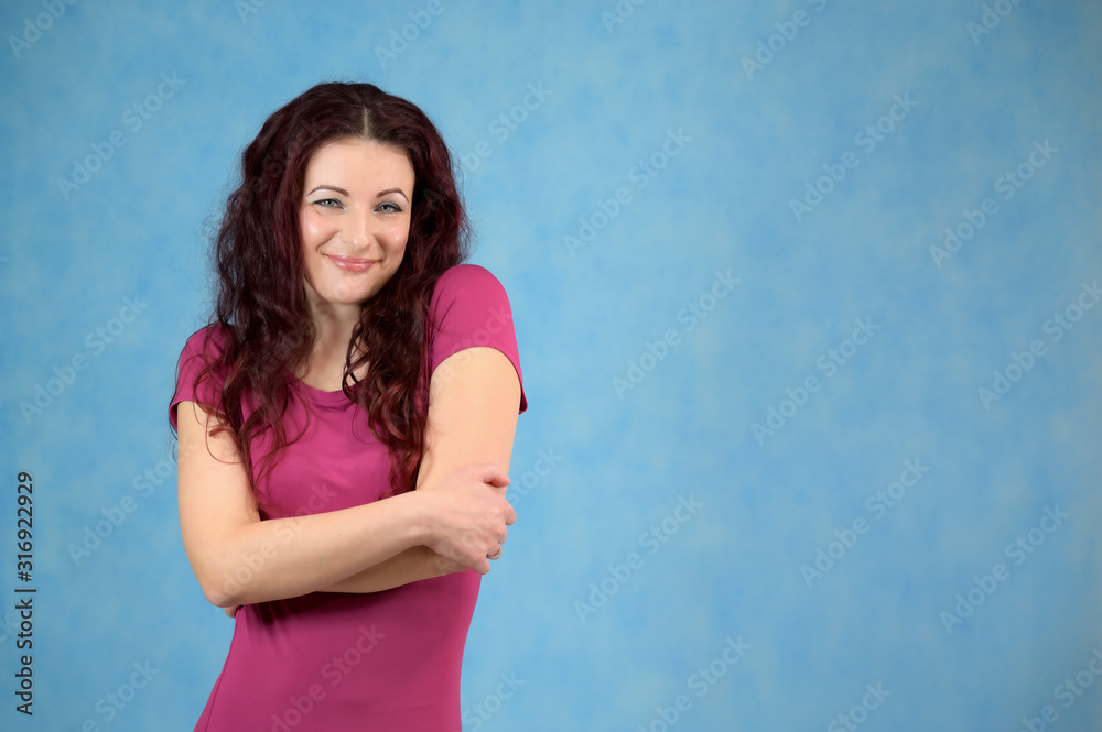 The model is smiling and talking cute to the camera. Portrait of a pretty slim brunette woman with emotions in a pink dress and with brown hair on a blue background in the studio. The model is smiling and talking cute to the camera. Portrait of a pretty slim brunette woman with emotions in a pink dress and with brown hair on a blue background in the studio.
