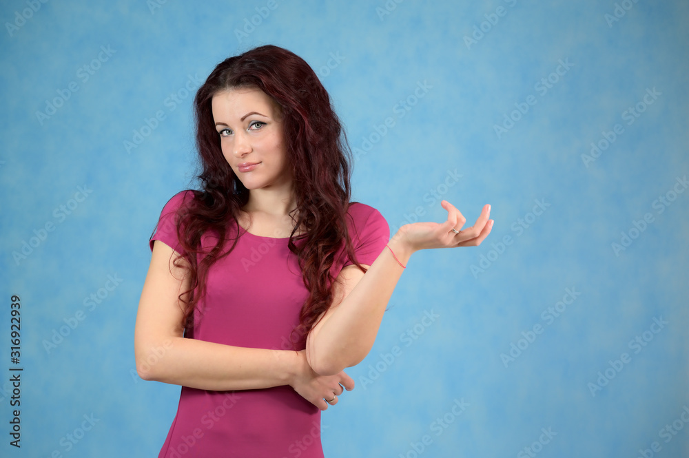 The model is smiling and talking cute to the camera. Portrait of a pretty slim brunette woman with emotions in a pink dress and with brown hair on a blue background in the studio. The model is smiling and talking cute to the camera. Portrait of a pretty slim brunette woman with emotions in a pink dress and with brown hair on a blue background in the studio.