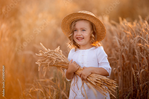 beautiful cheerful girls in a white dress and wicker boater hat on a wheat field in the rays of the setting sun. girl holding a bunch of ears of wheat