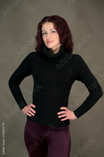 Portrait of a pretty slender brunette woman in a dark sweater and with brown hair stands on a gray background in the studio. The concept of fashionable art portrait of a glamorous model