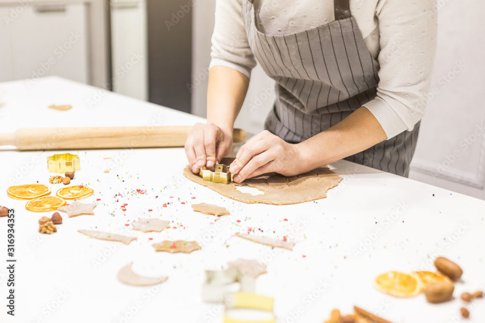 Young pretty woman prepares the dough and bakes gingerbread and cookies in the kitchen. She makes a star shape on the dough. Merry Christmas and Happy New Year. Young pretty woman prepares the dough and bakes gingerbread and cookies in the kitchen. She makes a star shape on the dough. Merry Christmas and Happy New Year.