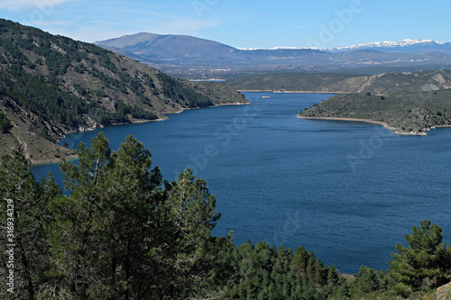 Natural landscape with reservoir and trees in the foreground, mountains in the background and intense blue sky, El Atazar reservoir, Madrid, Spain