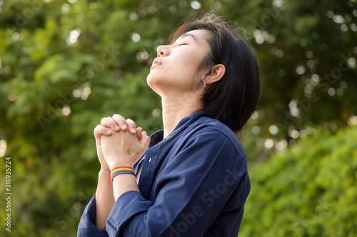 confident LGBT woman praying with rainbow ribbon symbol; concept of LGBT pride, LGBTQ people, lgbt rights wish, hope for equality, same sex marriage, sex preference diversity in modern society