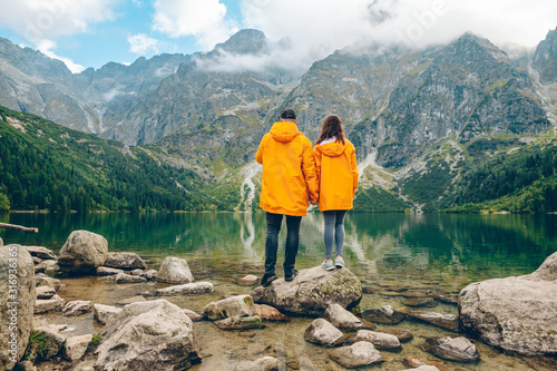 man with woman in yellow raincoat at sunny autumn day looking at lake in tatra mountains
