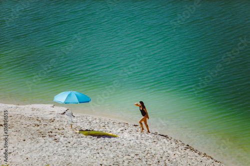 Fototapeta Naklejka Na Ścianę i Meble -  woman in swimsuit walking by sand beach blue sun umbrella and yellow blanket