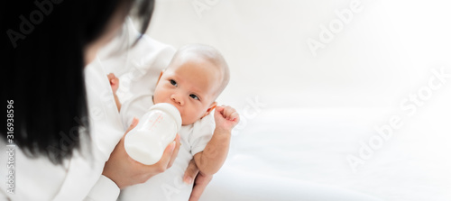Mother feeding asian baby with bottle of milk, banner copy space