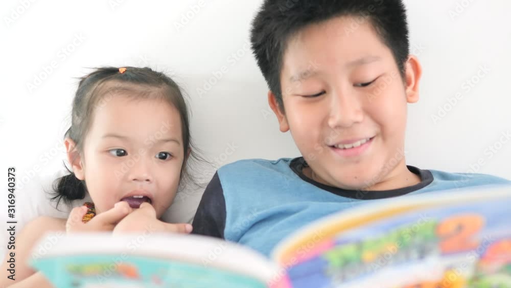 Asian boy reading a book for his sister at home. Asian boy reading a book for his sister at home.
