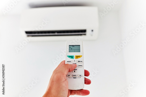 Modern air conditioner unit with a hand holding a remote.