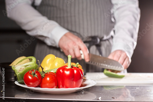 Closeup of hand with knife cutting fresh vegetable. Young chef cutting beet on a white cutting board closeup. Cooking in a restaurant kitchen