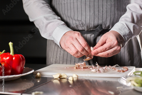 Closeup of hand with knife cutting fresh vegetable. Young chef cutting garlic on a white cutting board closeup. Cooking in a restaurant kitchen