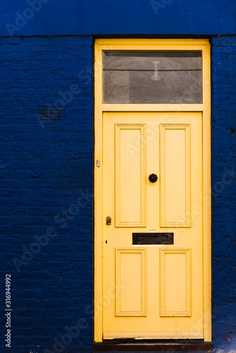 Closed wooden door painted in yellow on traditional brick facade painted in blue photo