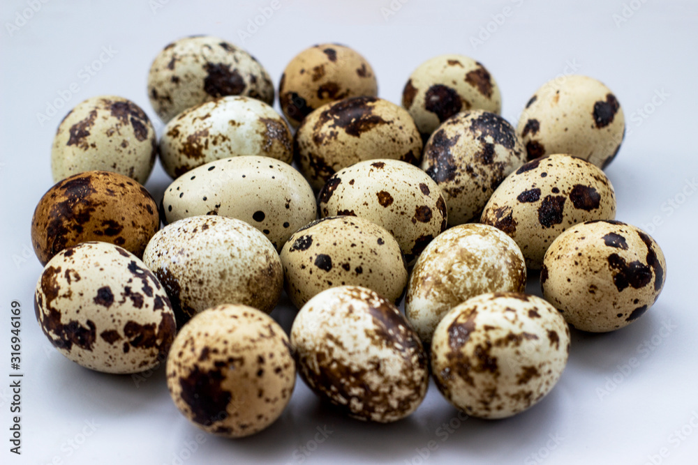Group of quail eggs on a white background. A lot of spotted eggs on a light background, close-up.