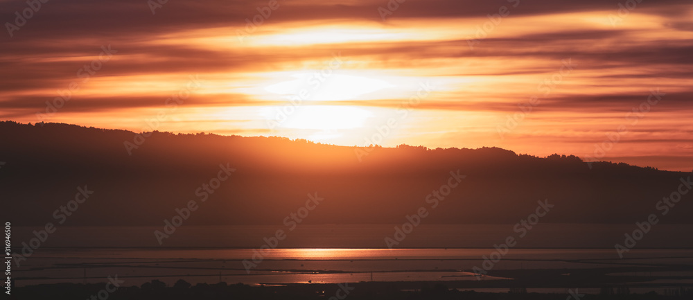 Sun setting behind the Santa Cruz mountains and reflected in the waters of San Francisco Bay; California