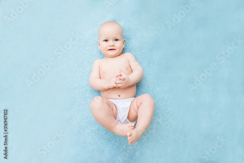 Calm curious baby lying on blue background, looking at camera, top view