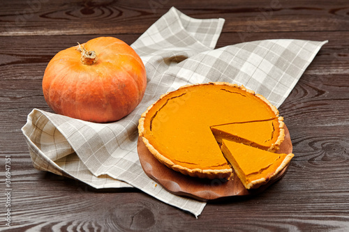 Thanksgiving pumpkin pie on cutting board on brown wooden table. Piece of pie