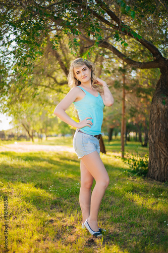 Beautiful girl on a walk in the park. Blonde in a blue t-shirt in the forest. Model with a cheerful smile
