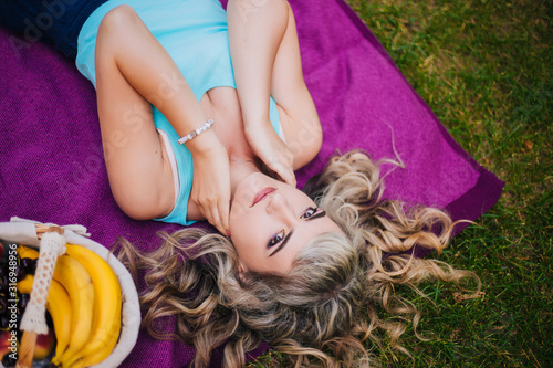 Beautiful girl on a picnic in the park. Blonde lying on a purple bedspread resting. Model with a cheerful smile