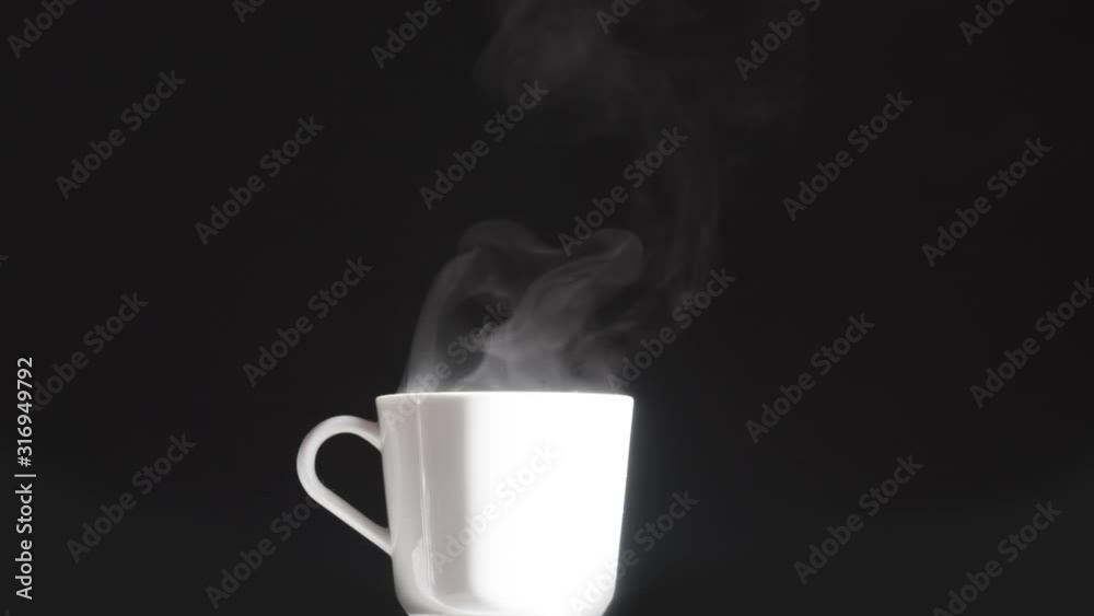 White Cup with a Hot Drink. Brightly lit white mug from which hot steam rises slowly on a black background White Cup with a Hot Drink. Brightly lit white mug from which hot steam rises slowly on a black background