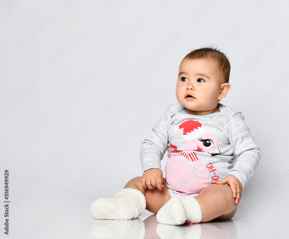 Little kid in socks and bodysuit with christmas flamingo print. She sitting on the floor isolated on white. Close up, copy space Little kid in socks and bodysuit with christmas flamingo print. She sitting on the floor isolated on white. Close up, copy space
