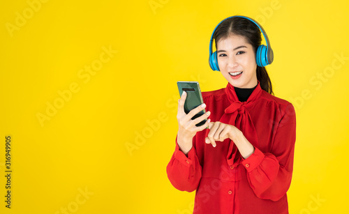 Asian women in the happy mood hold the phone and put the wireless headphone into the red dress. Choosing music from Mobile or studying E-leanning from mobile over yellow background with copy space.