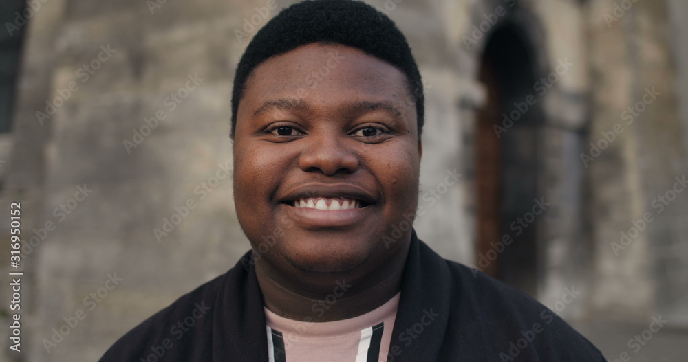Close up of excited man looking straight to camera. Young african male standing outdoors and smiling. Portraits. Daylight. Concept of people and emotions. Blurred background. Close up of excited man looking straight to camera. Young african male standing outdoors and smiling. Portraits. Daylight. Concept of people and emotions. Blurred background.