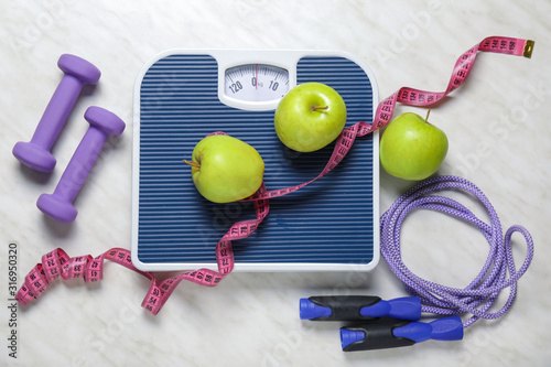 Apples, scales, dumbbells, jumping rope and measuring tape on light background. Diet concept