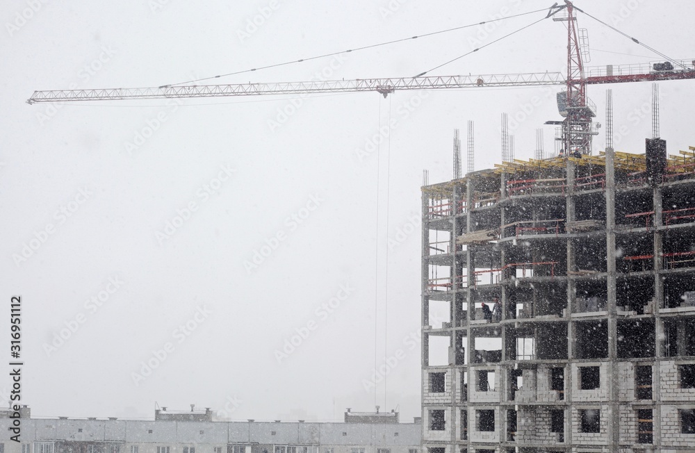 home building with crane on gray sky background in snowy weather home building with crane on gray sky background in snowy weather